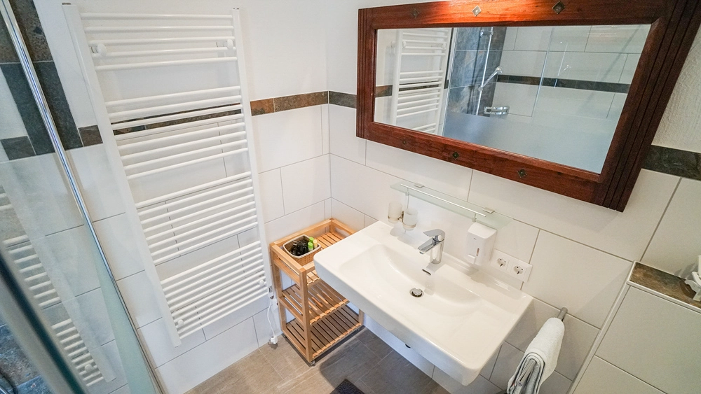 „Hahns Herberge“ – Innenansicht - Badezimmer; harmonische Farb- und Materialgestaltung, Spiegel, Waschbecken und Handtuchhalter.